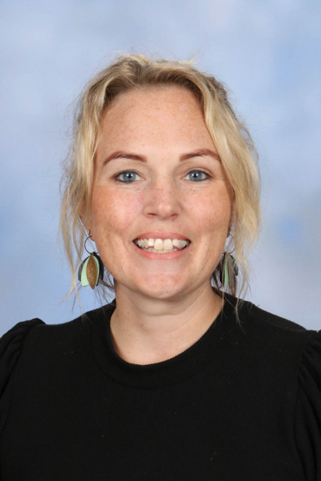 Headshot of Amy wearing leaf-shaped earrings and a black top.