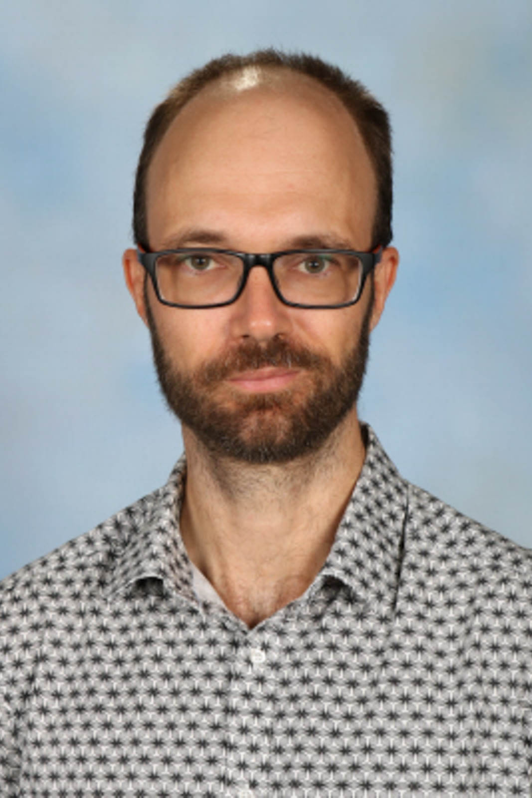 Headshot of Thomas in a dot-patterned shirt and glasses.