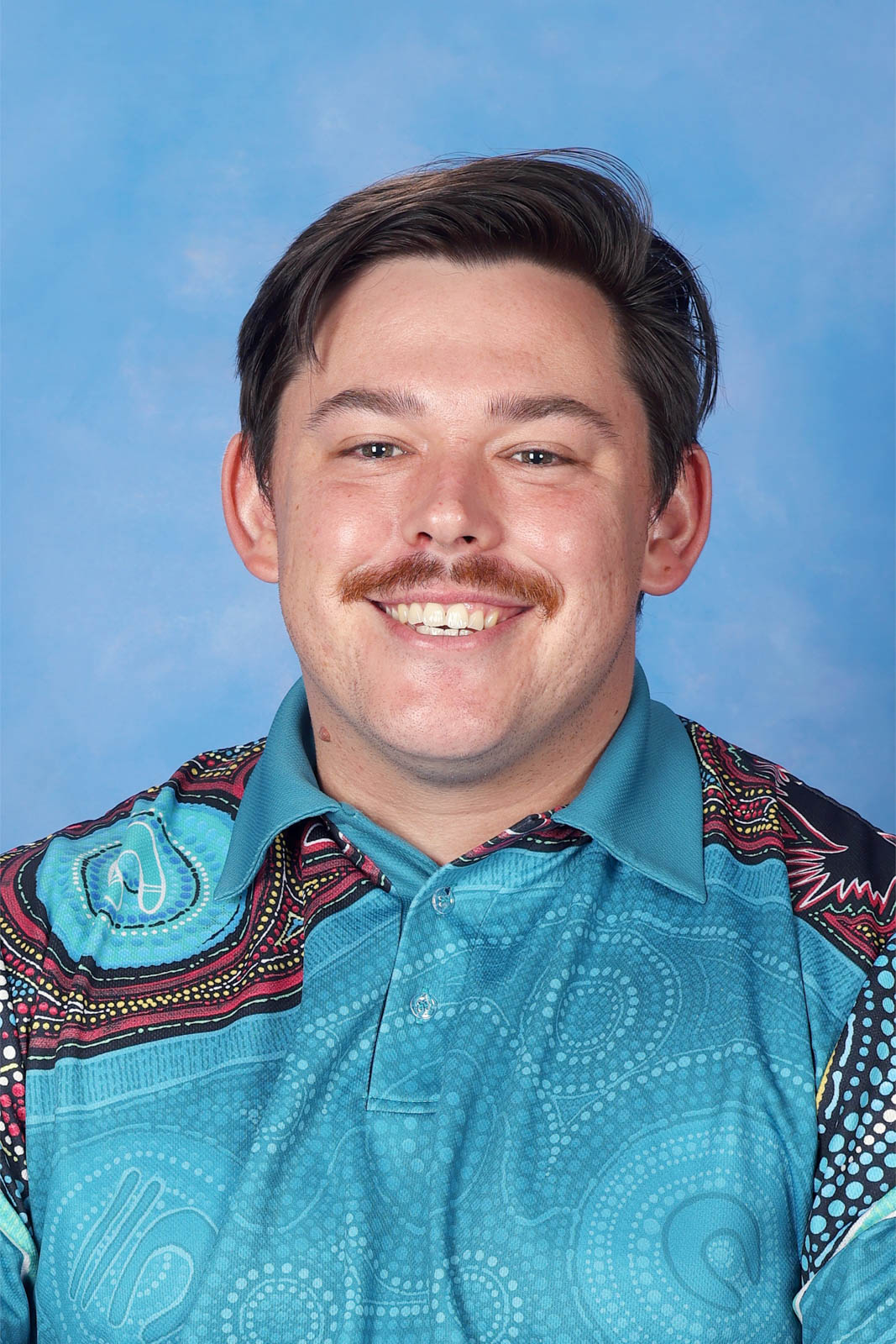 Headshot of Alex in a polo with indigenous patterns.