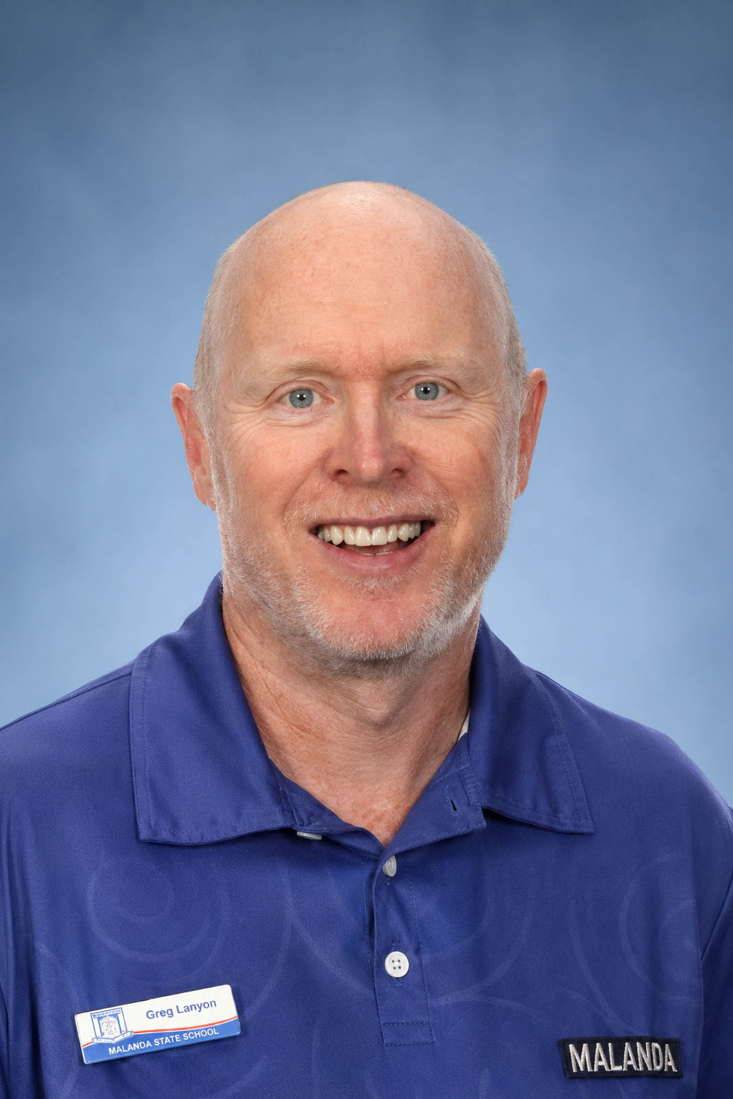 Headshot of Greg in a blue polo wearing a name badge.